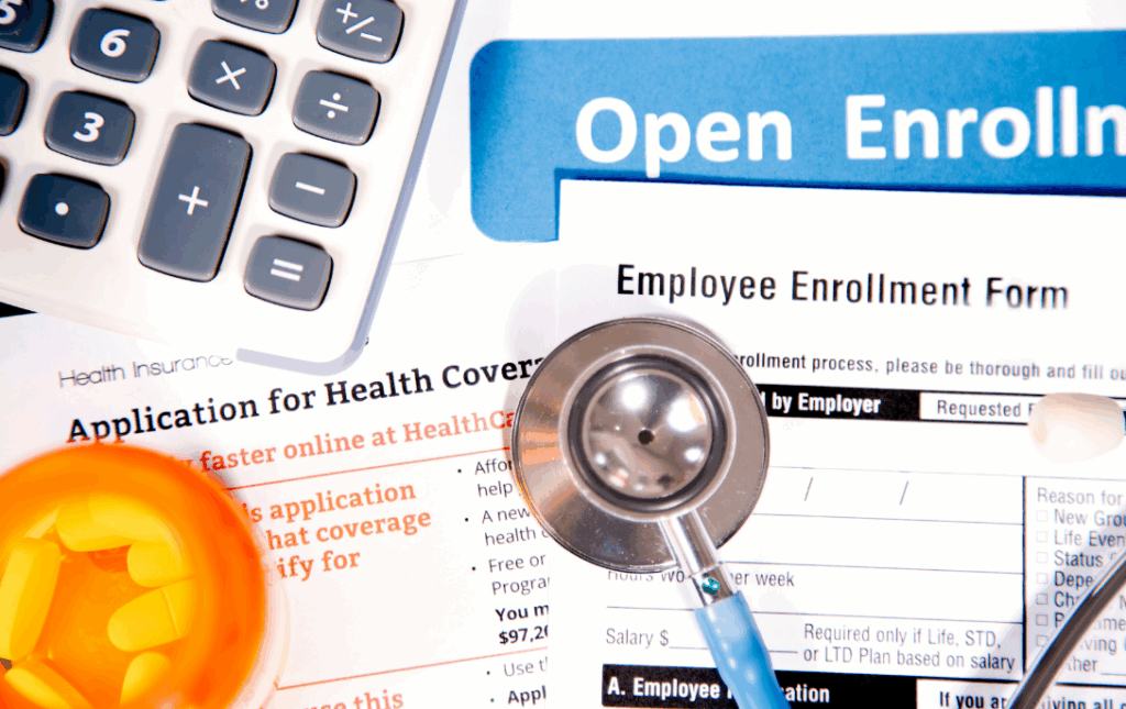Stethoscope, Calculator and pill bottle over Open Enrollment Forms,
