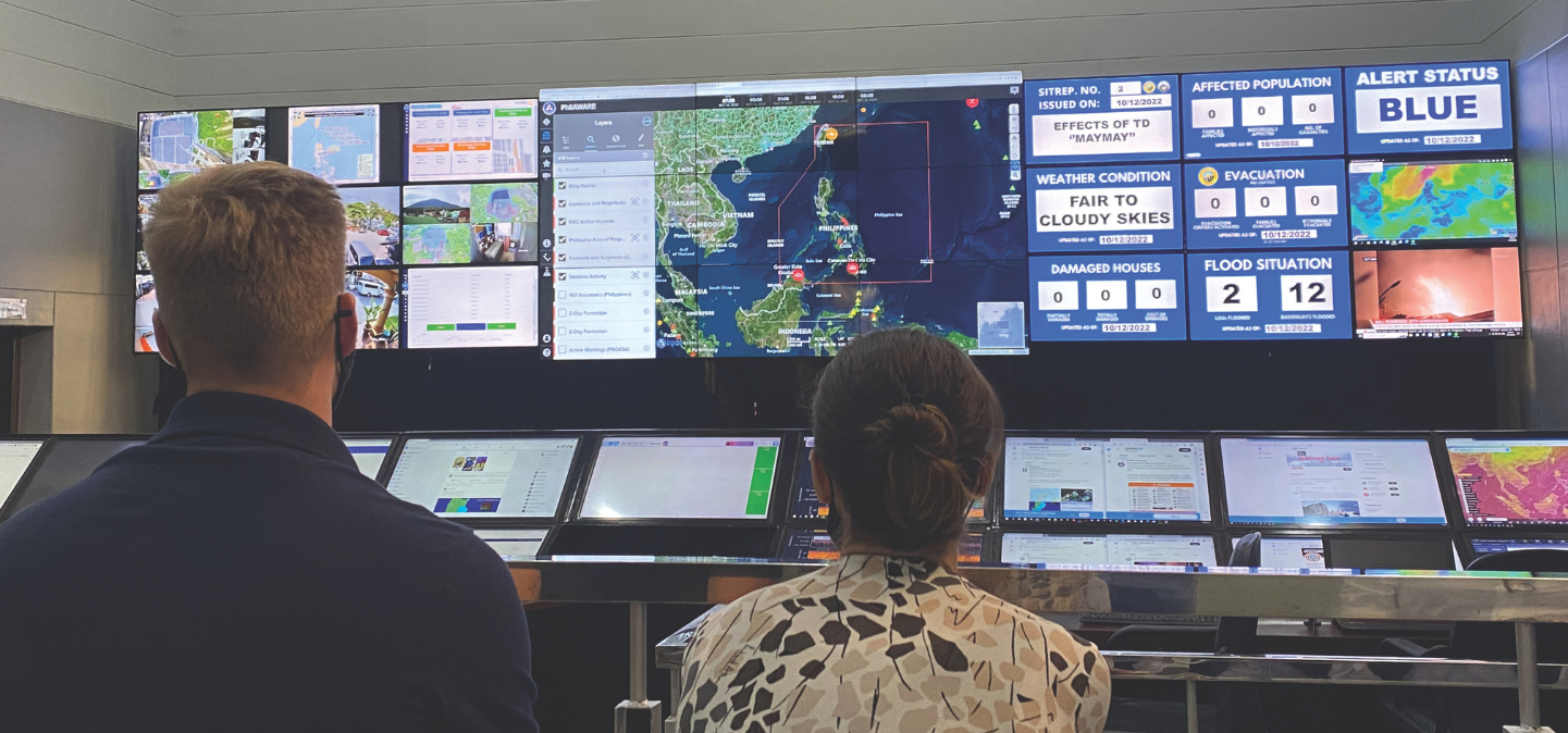The back of a man and woman looking at screens of a map and weather conditions