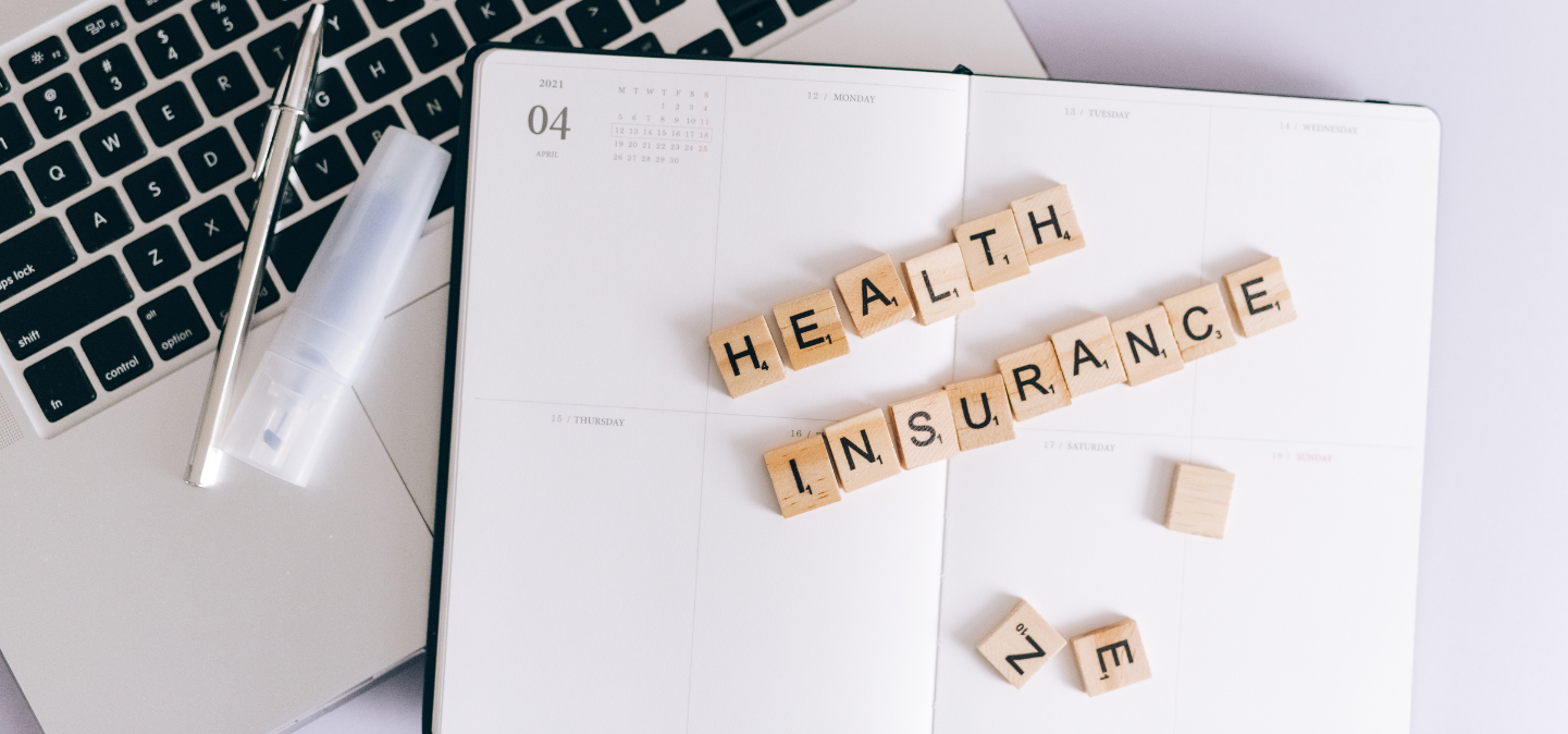 Health Insurance spelled in Scrabble pieces over a calendar and laptop