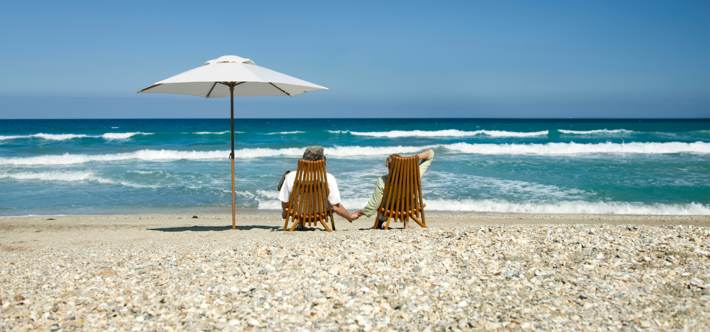Two people holding hands and sitting on a beach under an umbrella